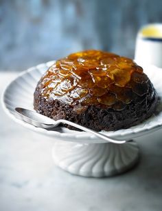 a cake on a white plate with a fork and cup in the backgroud