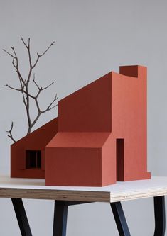 an orange house sitting on top of a wooden table next to a bare tree with no leaves