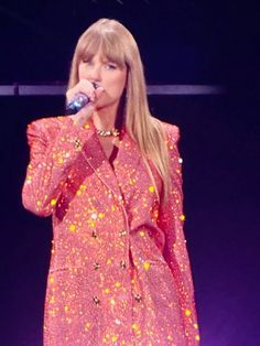 taylor swift performing on stage with microphone in her hand and wearing a bright pink dress