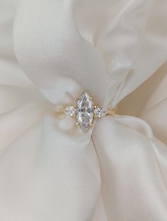 a diamond ring sitting on top of a white satin fabric with a flower in the middle