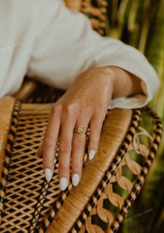 a woman's hand resting on a wicker chair with her nails painted white