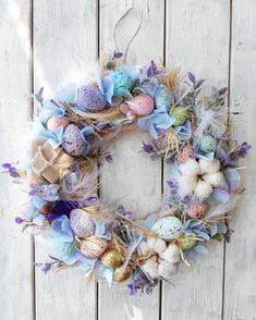 an easter wreath with eggs and feathers on a white wooden background, hanging from the wall