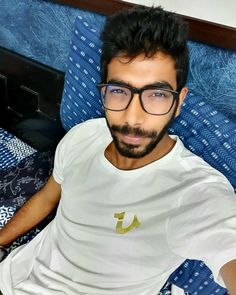 a man with glasses sitting on top of a bed next to a blue comforter