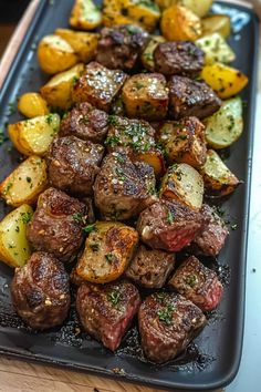 steak and potatoes are served on a black platter with seasoning sprinkles