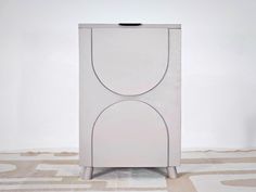 a white cabinet sitting on top of a floor next to a carpeted area with an abstract design