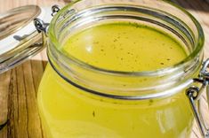 a jar filled with yellow liquid sitting on top of a wooden table next to a spoon