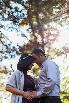 a man and woman standing next to each other in front of trees with the sun shining on them