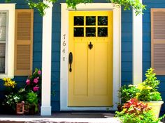 a blue house with yellow front door and shutters on the windows is decorated with potted plants