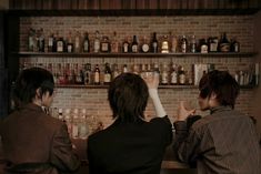 two people sitting at a bar with bottles on the shelves