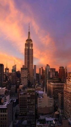 the empire building in new york city is lit up at sunset with pink and yellow clouds