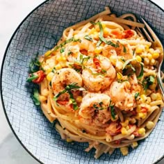 a bowl filled with pasta and shrimp on top of a marble countertop next to a fork