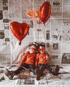 two young boys wearing red heart shaped glasses sitting on newspaper with balloons in the air