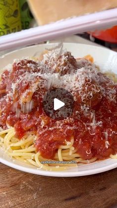 a white plate topped with spaghetti and meat covered in sauce on top of a wooden table