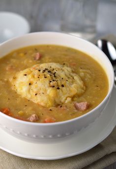 a white bowl filled with soup on top of a table next to a spoon and napkin