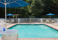 an empty swimming pool surrounded by chairs and umbrellas with trees in the back ground