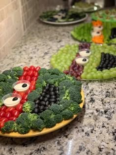 two plates with fruit and vegetables shaped like faces on them sitting on a kitchen counter