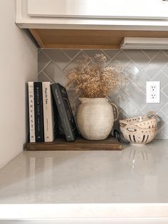 a vase with flowers and books sitting on a shelf in a kitchen next to a light switch