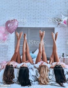 three women laying in bed with their feet up on the covers and balloons flying above them