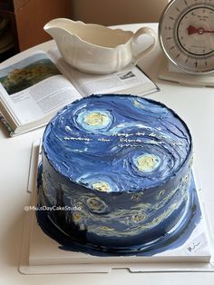 a cake that looks like the starry night is on top of a table next to an open book