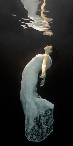 a woman is floating in the water wearing a white dress