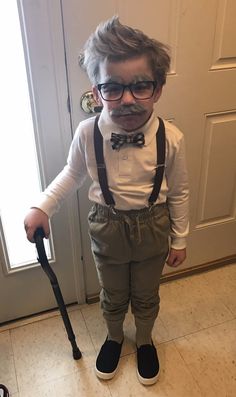 a little boy wearing glasses and suspenders with a cane in front of a door