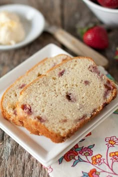 two slices of cake on a white plate with strawberries in the bowl behind it