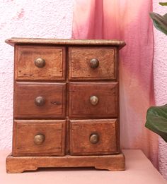 an old wooden chest of drawers on a pink shelf next to a potted plant