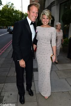 a man in a tuxedo standing next to a woman in a dress on a sidewalk