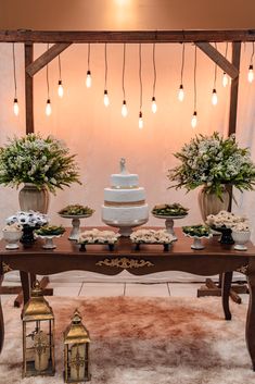 a wedding cake sits on top of a table surrounded by vases and flowers with lights hanging above it