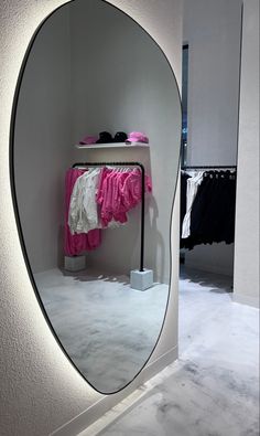 a mirror that is reflecting clothes on a rack in a room with white walls and flooring