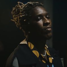 a young man with dreadlocks stares into the distance while wearing a yellow and black shirt