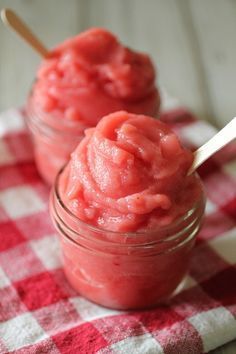 two jars filled with red food sitting on top of a checkered table cloth next to a spoon