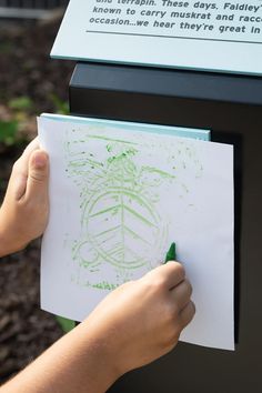 a person holding a piece of paper with green ink on it next to a sign