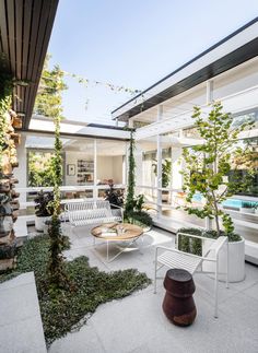 an outdoor living area with white furniture and greenery on the side of the building