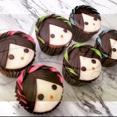 six cupcakes with chocolate frosting decorated to look like women's faces