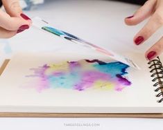 a woman is painting with watercolors on an open notebook