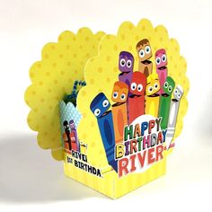 a birthday card with colorful crayons in a box on a white tablecloth