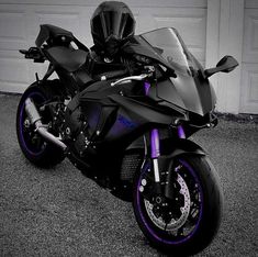 a black and purple motorcycle parked in front of a garage with a helmet on it's head