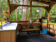 an outdoor kitchen area in the woods with lots of wood furniture and accessories on it