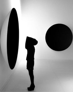 a person standing in front of two black and white circular shapes on the wall with their hands behind their head