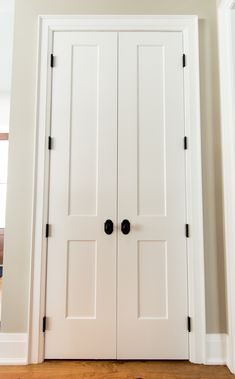 two white doors with black knobs in a home's entryway and hardwood flooring