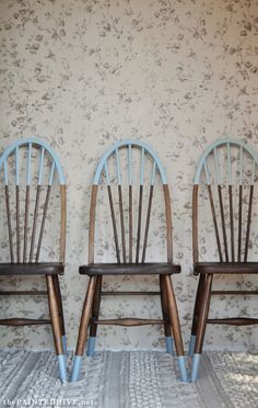 two wooden chairs sitting next to each other in front of a wallpapered background