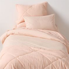 an unmade bed with peach colored sheets and pillow cases on top of it, against a white wall