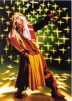 a man with long white hair is dancing in front of green and yellow stars on the wall