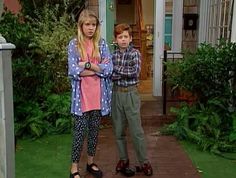 the young boy and girl are standing in front of their house with their arms crossed