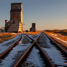 a train track with snow on the ground and an old building in the background