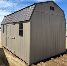 a storage shed sitting in the middle of a dirt field next to a blue sky