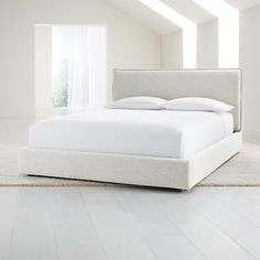 a white bed sitting in the middle of a room next to a wall with windows