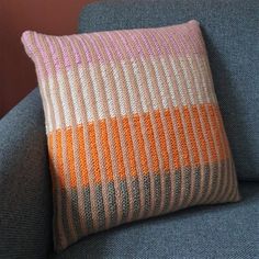 a blue couch with a knitted pillow on it's back and an orange stripe