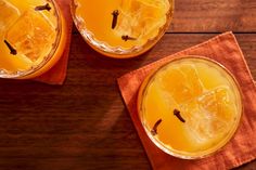 two glasses filled with orange juice sitting on top of a wooden table next to an orange napkin